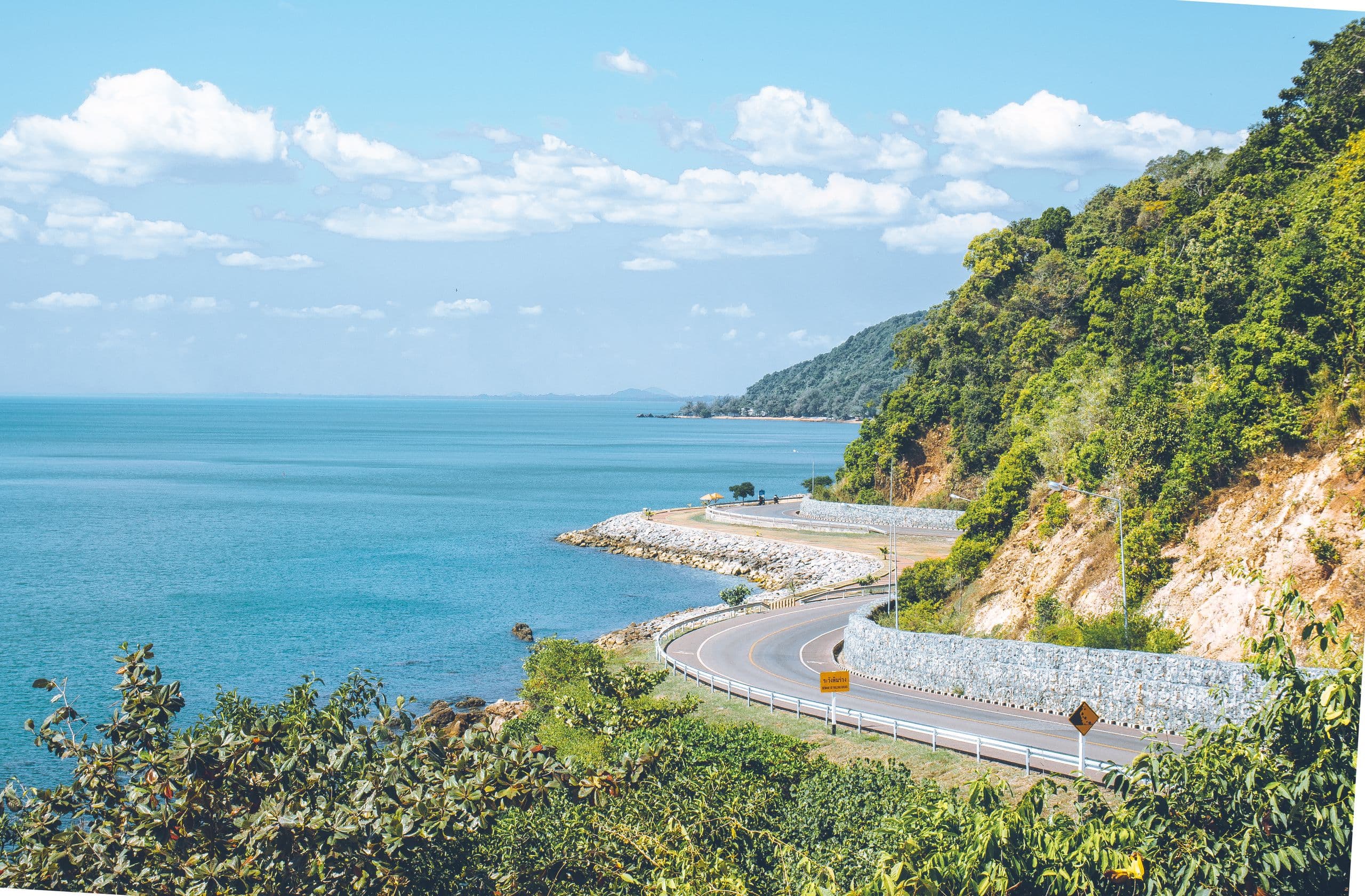 Eine Küstenstraße im Süden Thailands, die sich unterhalb bewaldeter Hügel am Ufer entlangzieht